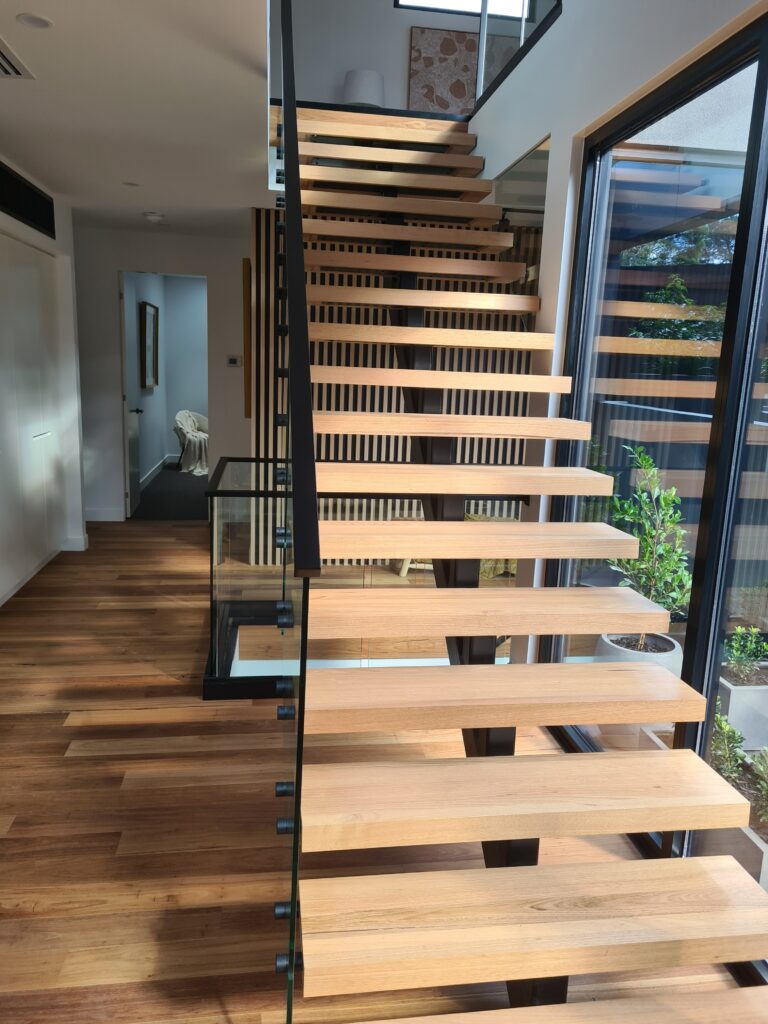 Floating timber stair treads on hidden steel stringers beside a glass balustrade