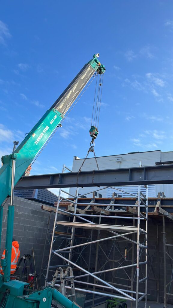 Crane lifting a structural steel beam into place on a commercial building site