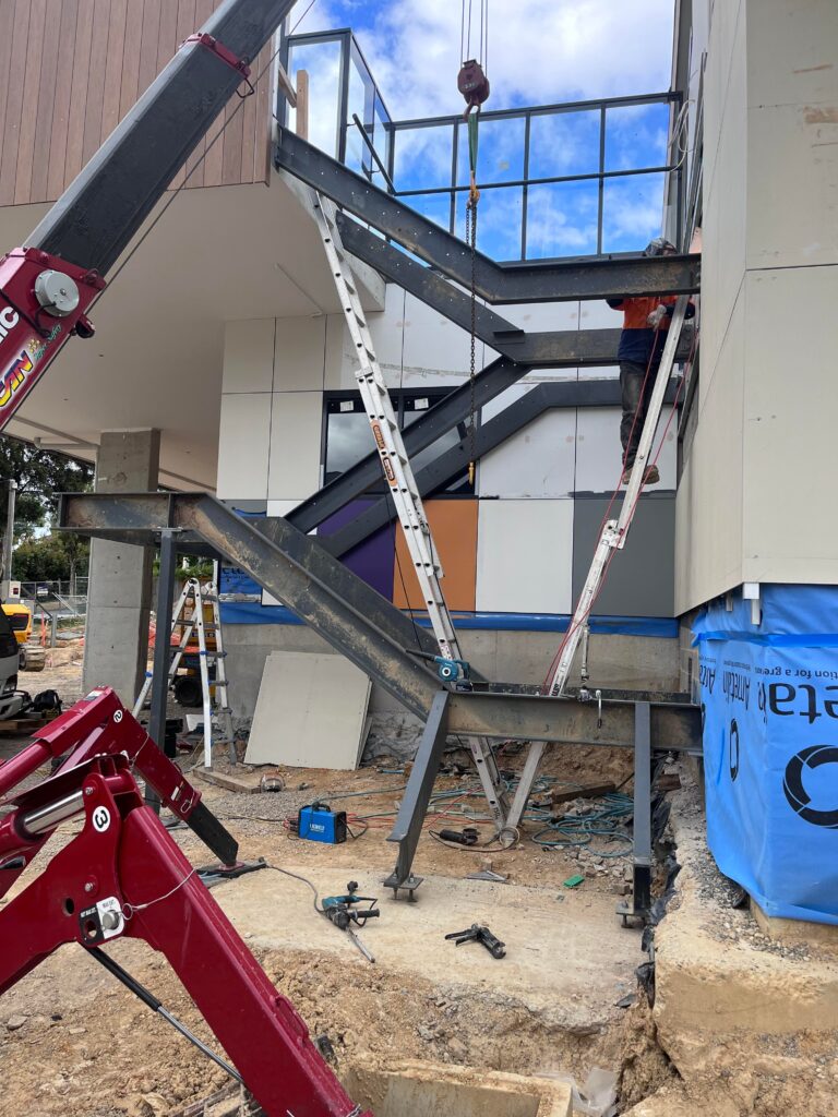 Steel stair stringers being lifted into place by crane on a multi-storey building in Heathmont