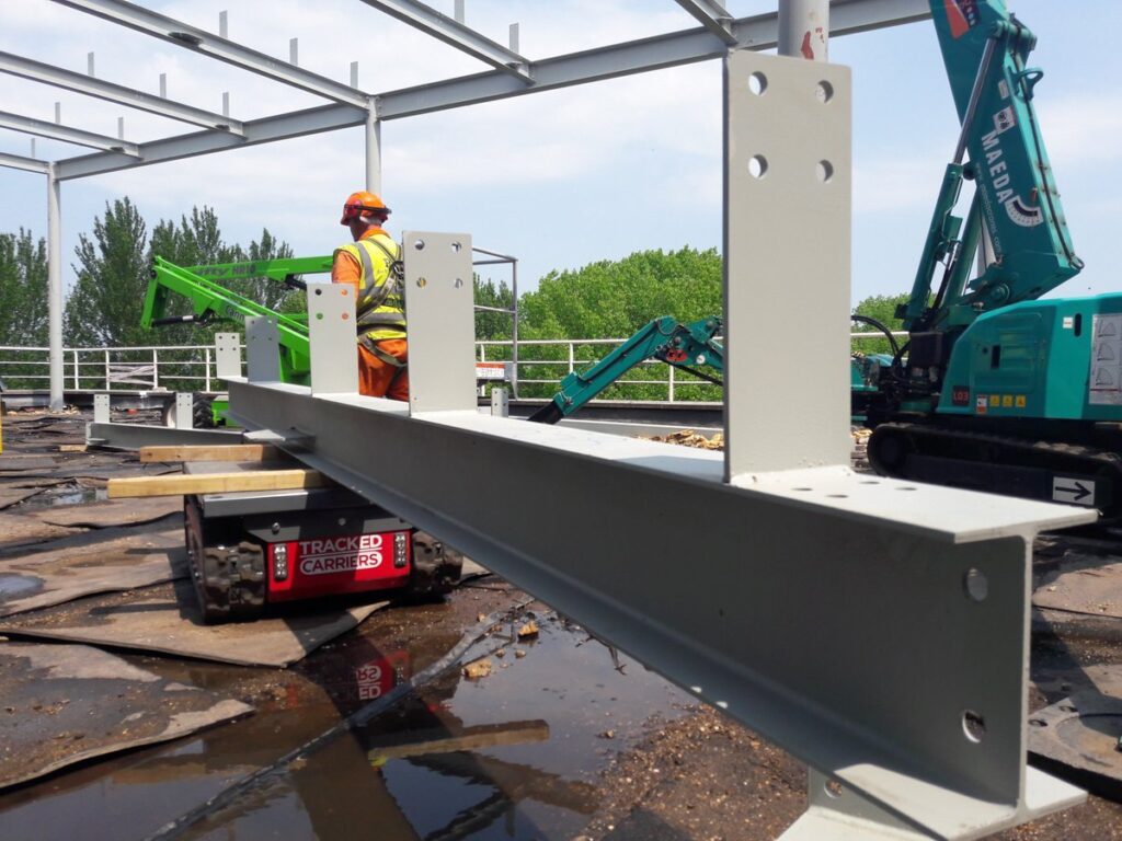 Fabricated steel beam with welded connection plates on a tracked carrier at a building site